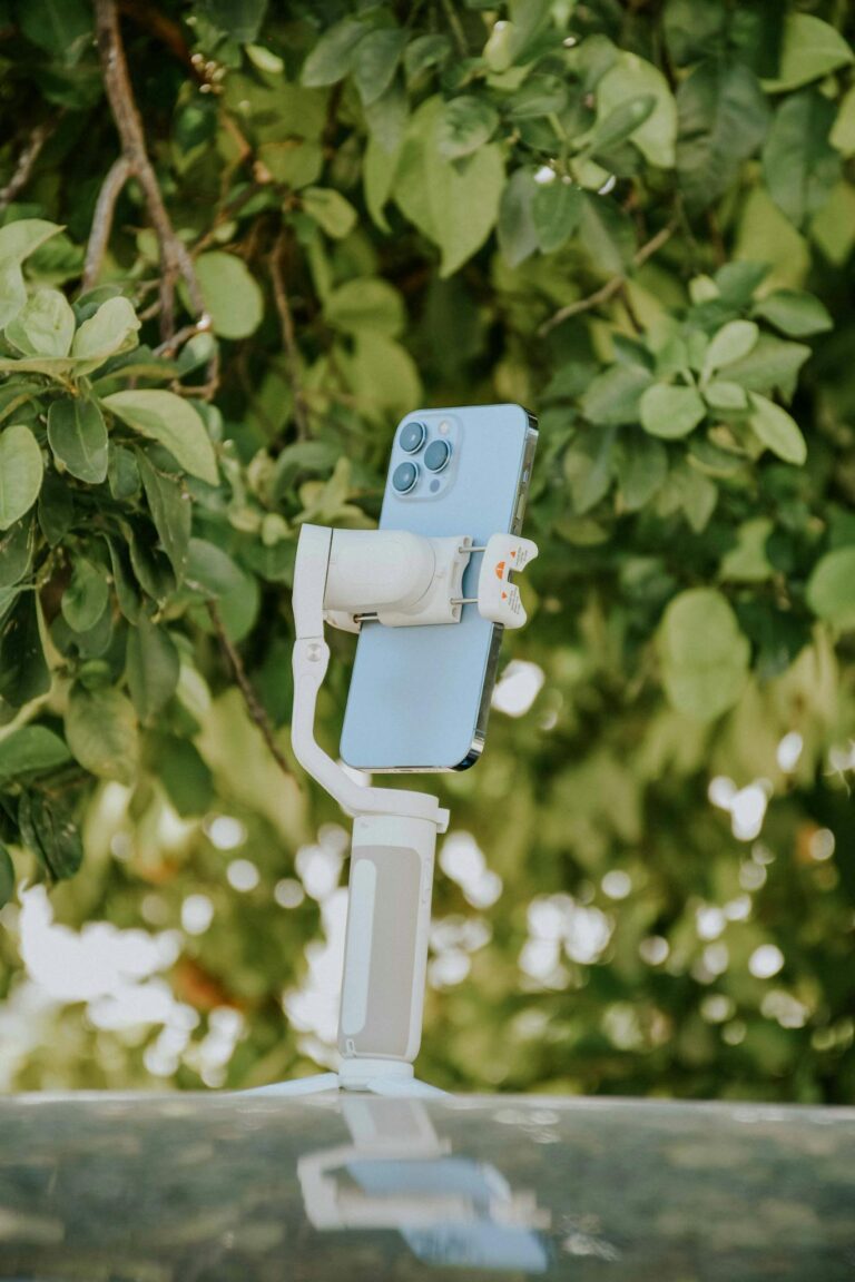A smartphone mounted on a stabilizer against a lush green backdrop, showcasing outdoor use in photography.